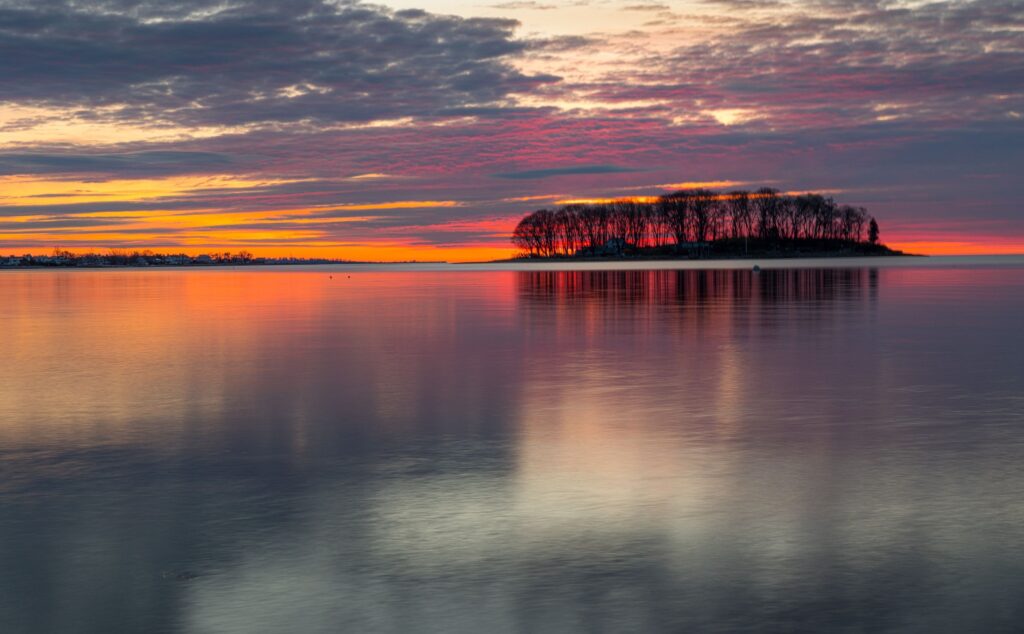 Picturesque view of the shoreline in Norwalk, Connecticut with colorful sky reflecting in the ocean