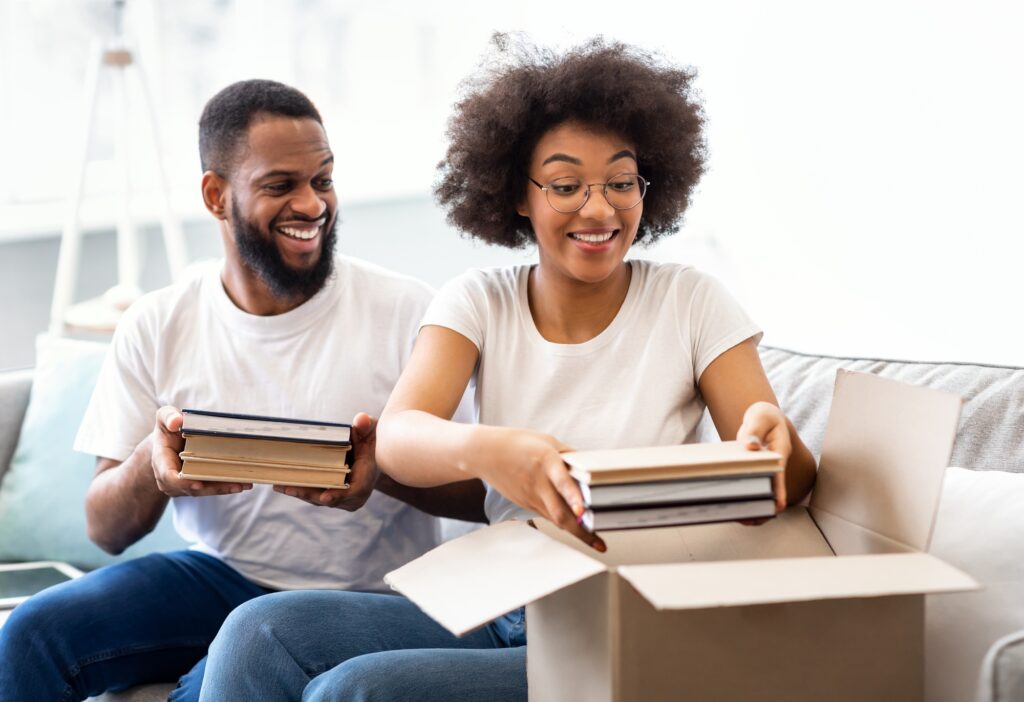 Black Spouses Packing Books In Boxes Moving To New Apartment